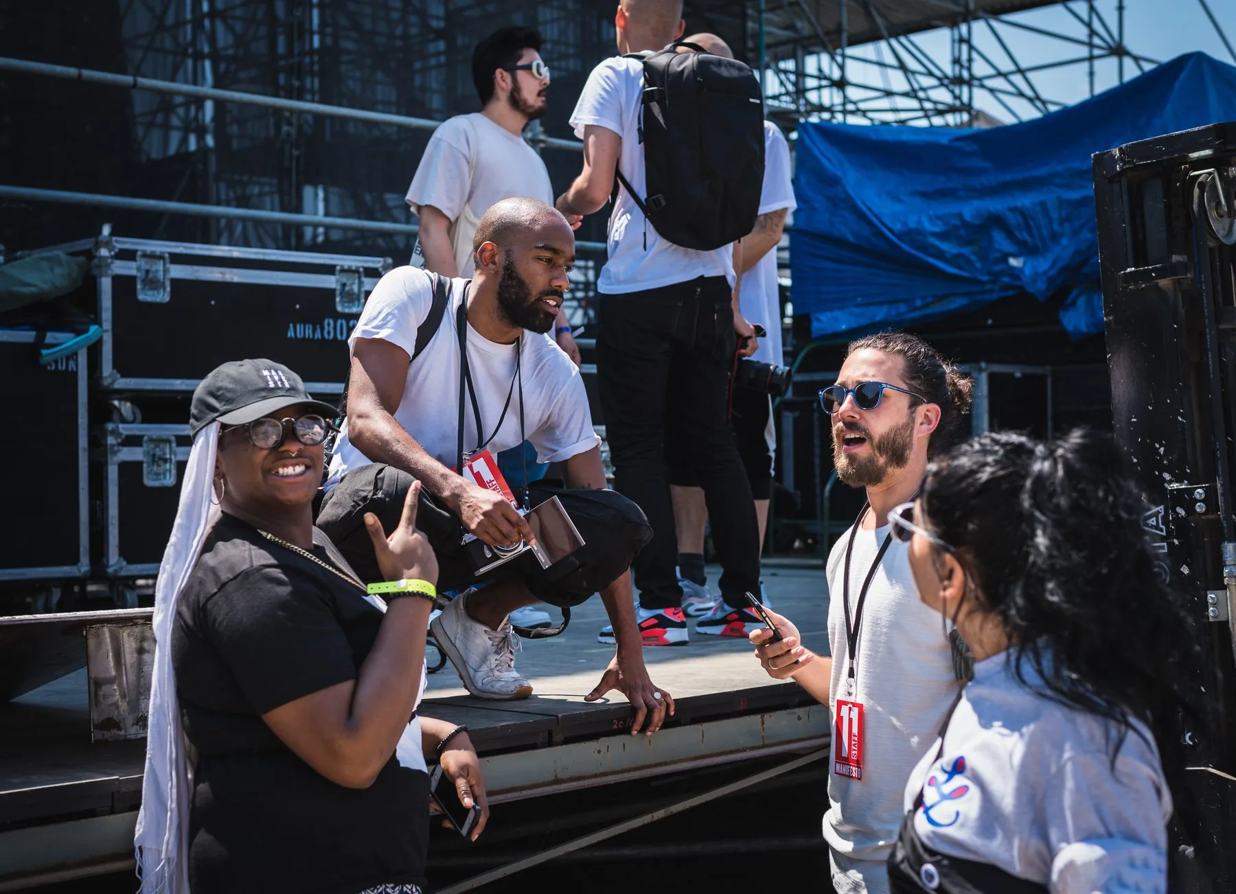 Documentation crew backstage at Echo Beach, staff laminates, road cases and a photographer crouched on the stage deck.